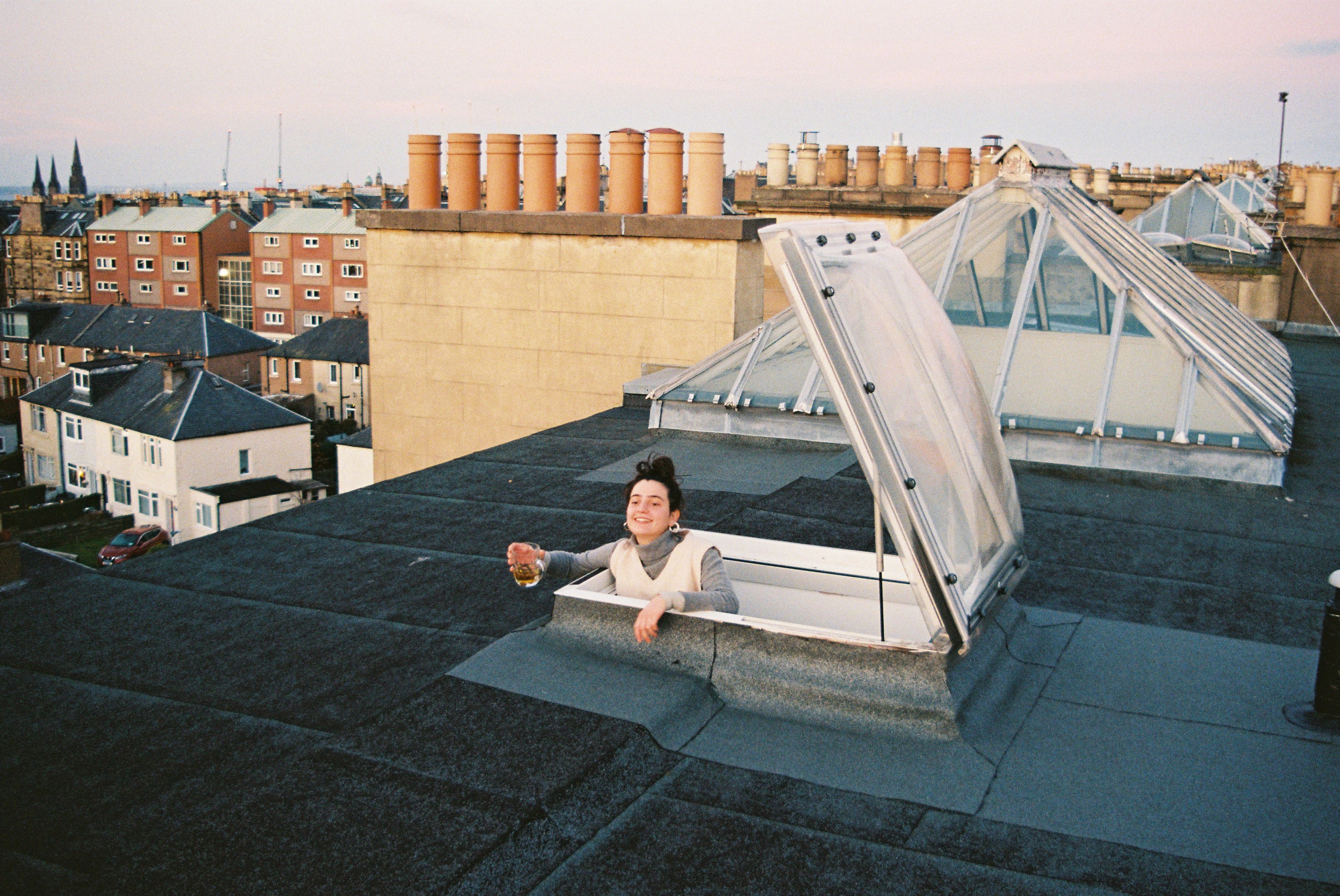 Hannah is popping out of the door to the roof with a drink in her hand